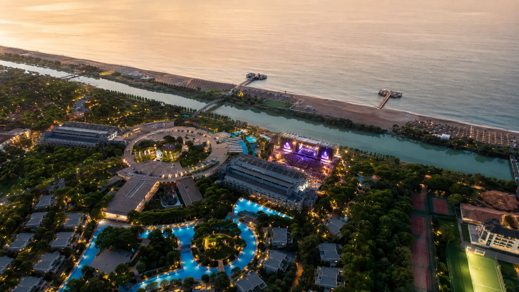 Вид с высоты на курорт Gloria Hotels & Resorts в Белеке с пляжем, бассейнами, зелёной территорией и концертной сценой.