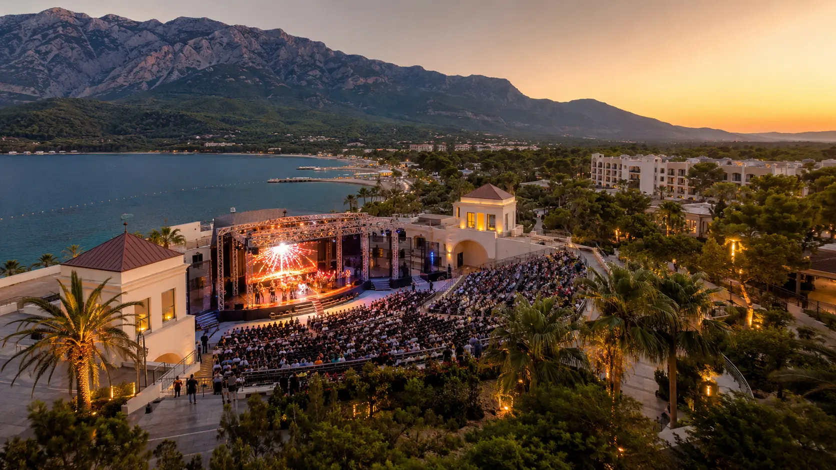 Вечерний концерт на открытой сцене отеля Rixos Sungate в Кемере с видом на море, горы и зрительный зал.
